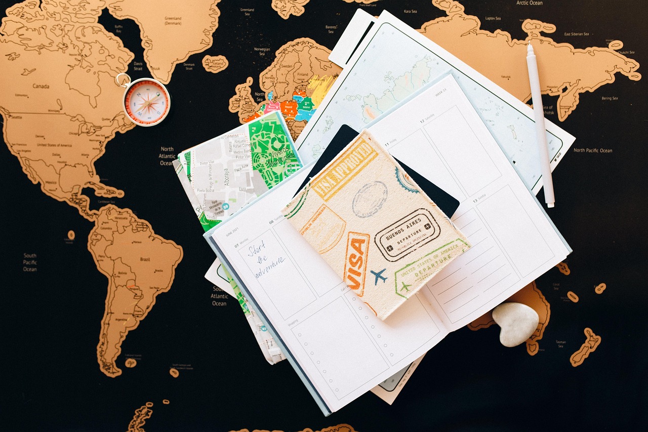 This article explains that visa fees for entering Japan are set to increase. The image shows a world map with a travel notebook, maps, and a passport cover decorated with visa stamps laid out on top.