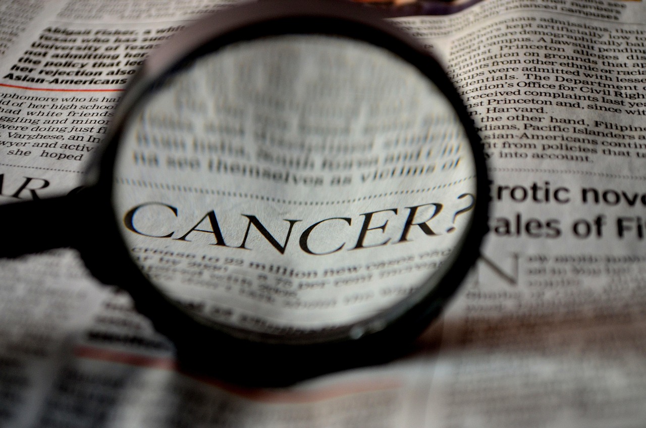 An eye-catch image showing the word “CANCER” magnified through a magnifying glass on a newspaper, indicating an article about cancer treatment, alongside news that Rakuten Medical has raised $100 million in a Series F funding round.